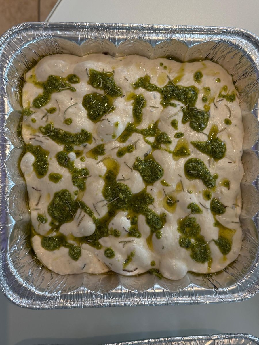 Focaccia dough dimpled and dressed with pesto and olive oil before baking